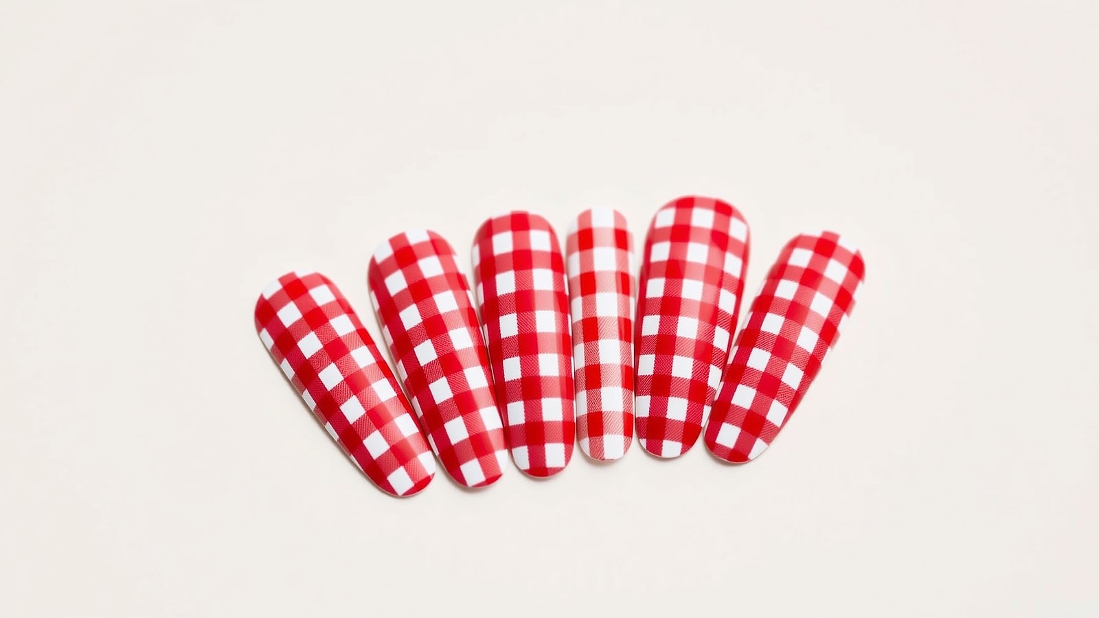 Macro of hand-painted red-and-cream gingham nail art on short round nails