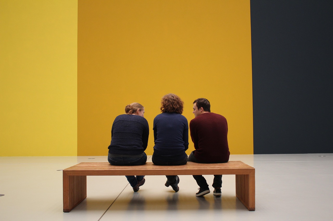 Three visitors on a wooden bench before large yellow and black colour-field works
